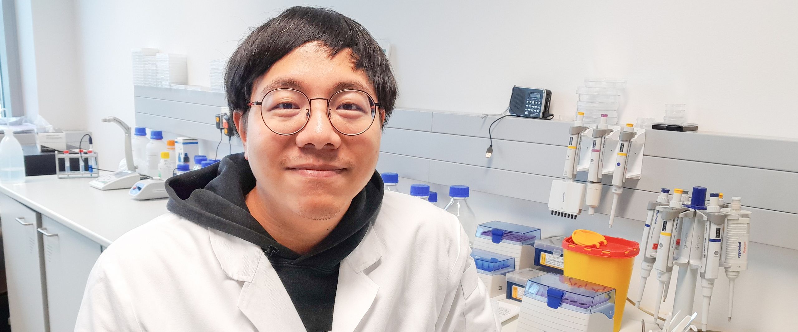 Mann sitz im weißen Kittel im Labor und lächelt in die Kamera