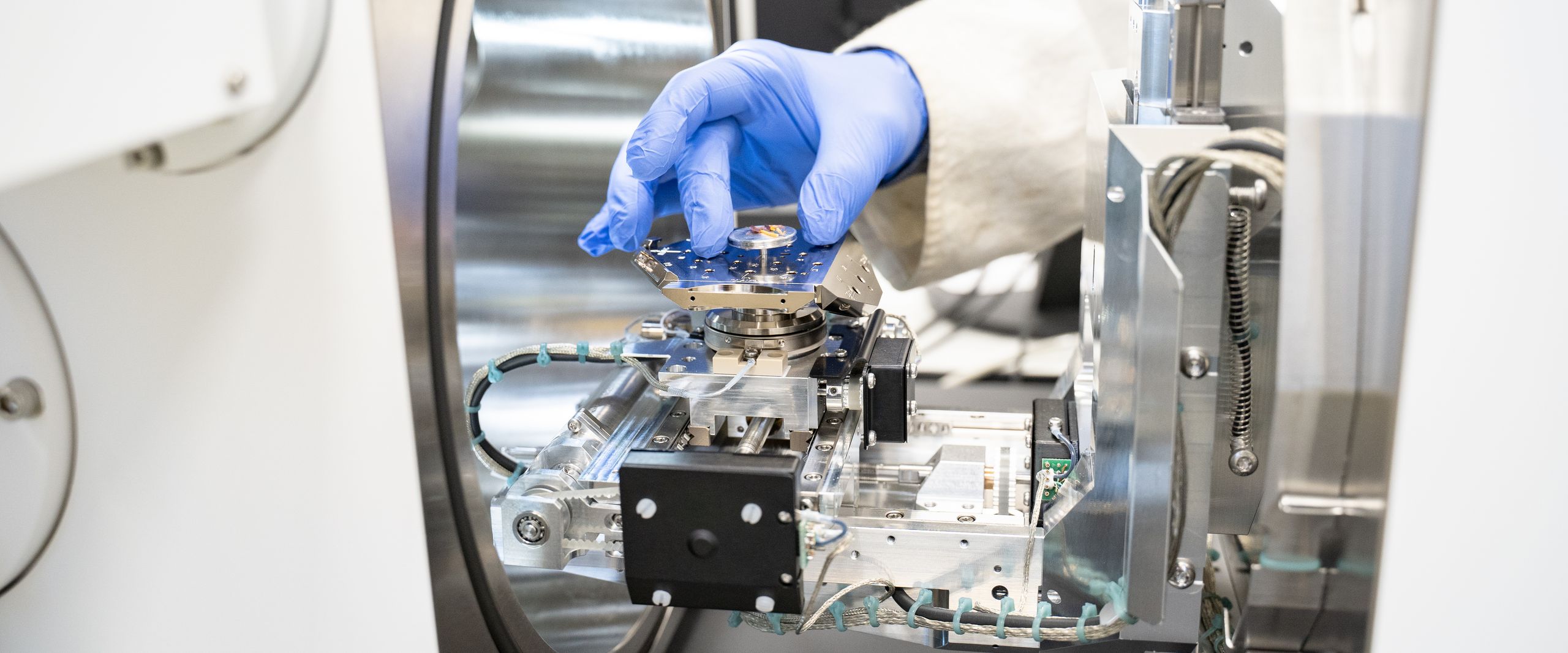 DFG-Gerätezentrum Probe Bld zeigt Hand mit blauem Handschuh, die eine Probe in einem kleinen Behälter zeigt.