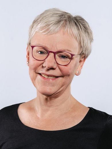 Auf dem Foto ist Annette Harth zusehen. Sie hat kurze graue Haare und trägt eine rote Brille und ein schwarzes Shirt. 