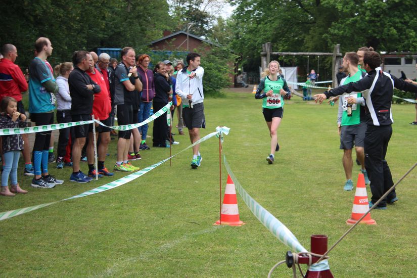 Zuschauer stehen neben der Laufstrecke und schauen einer L&auml;uferin zu.