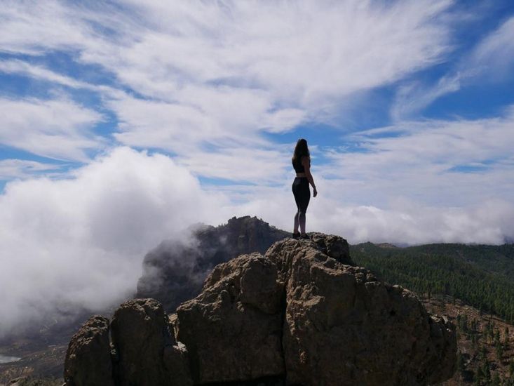 Ein Stein auf der Spitze eines Berges ist der Aussichtspunkt für eine junge Frau, deren Silhouette sich vor der Aussicht und den Wolken abzeichnet. 