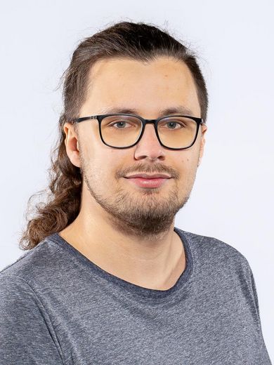 Auf dem Bild ist Christopher Lausch zusehen. Er hat lange braune Haare und einen Drei-Tage-Bart. Er tr&auml;gt eine Brille und ein blaues T-Shirt. 