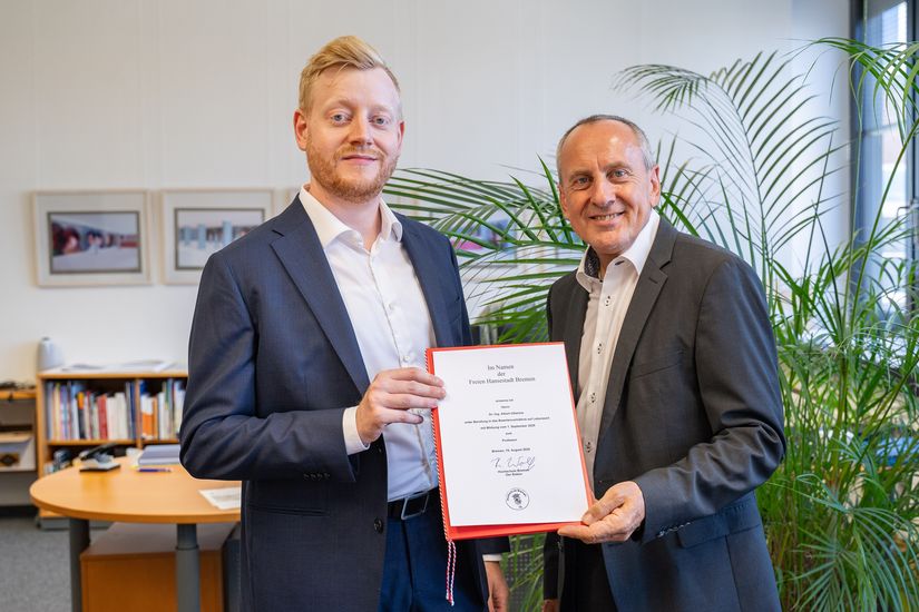 Zwei M&auml;nner halten gemeinsam eine Urkunde und schauen in die Kamera