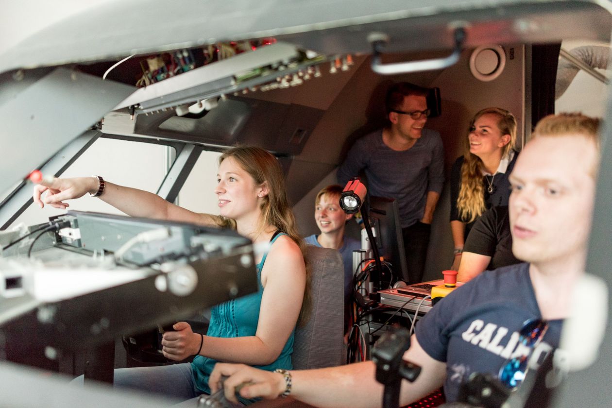 Junge Männer und Frauen sitzen im Cockpit eines Flugsimulators. 