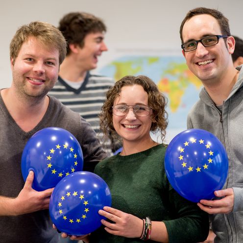 Zwei junge M&auml;nner und eine junge Frau halten dunkelblaue Luftballons mit den EU-Sternen und lachen in die Kamera.