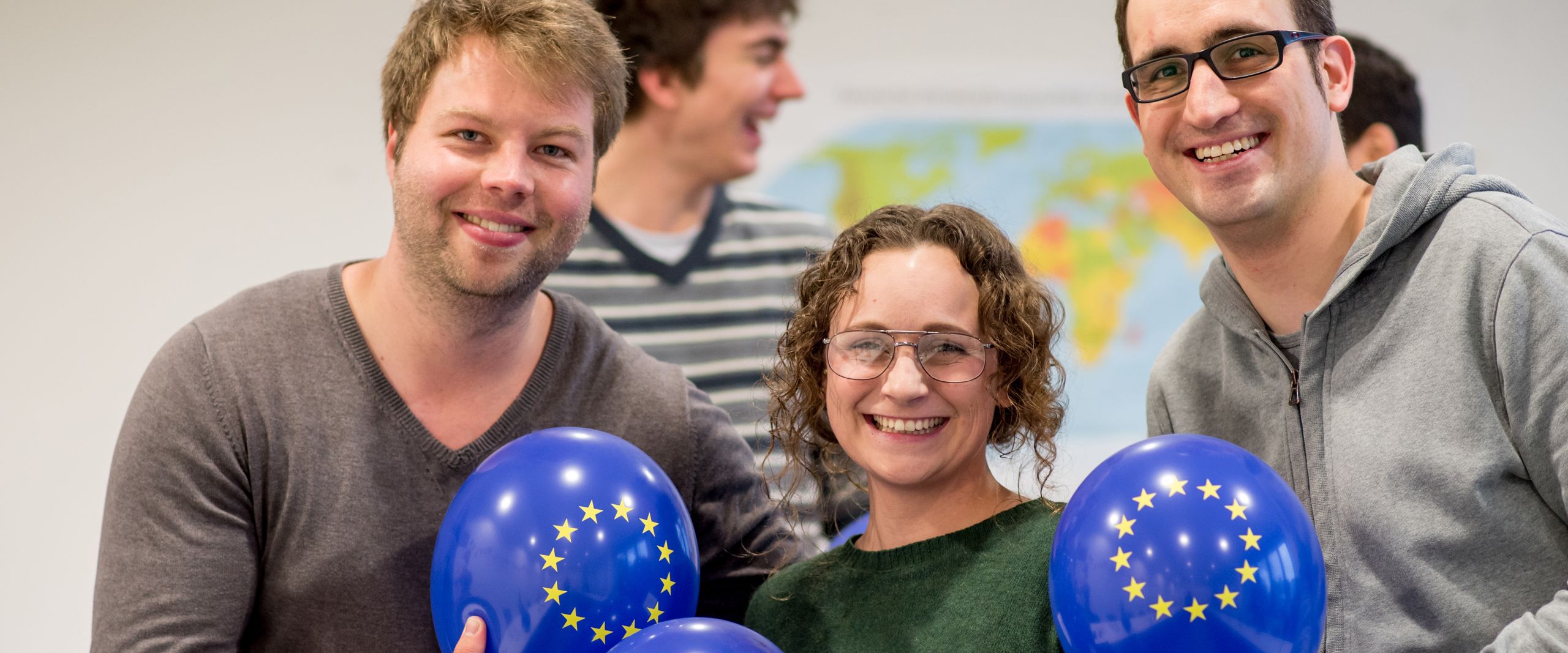 Zwei junge Männer und eine junge Frau halten dunkelblaue Luftballons mit den EU-Sternen und lachen in die Kamera.