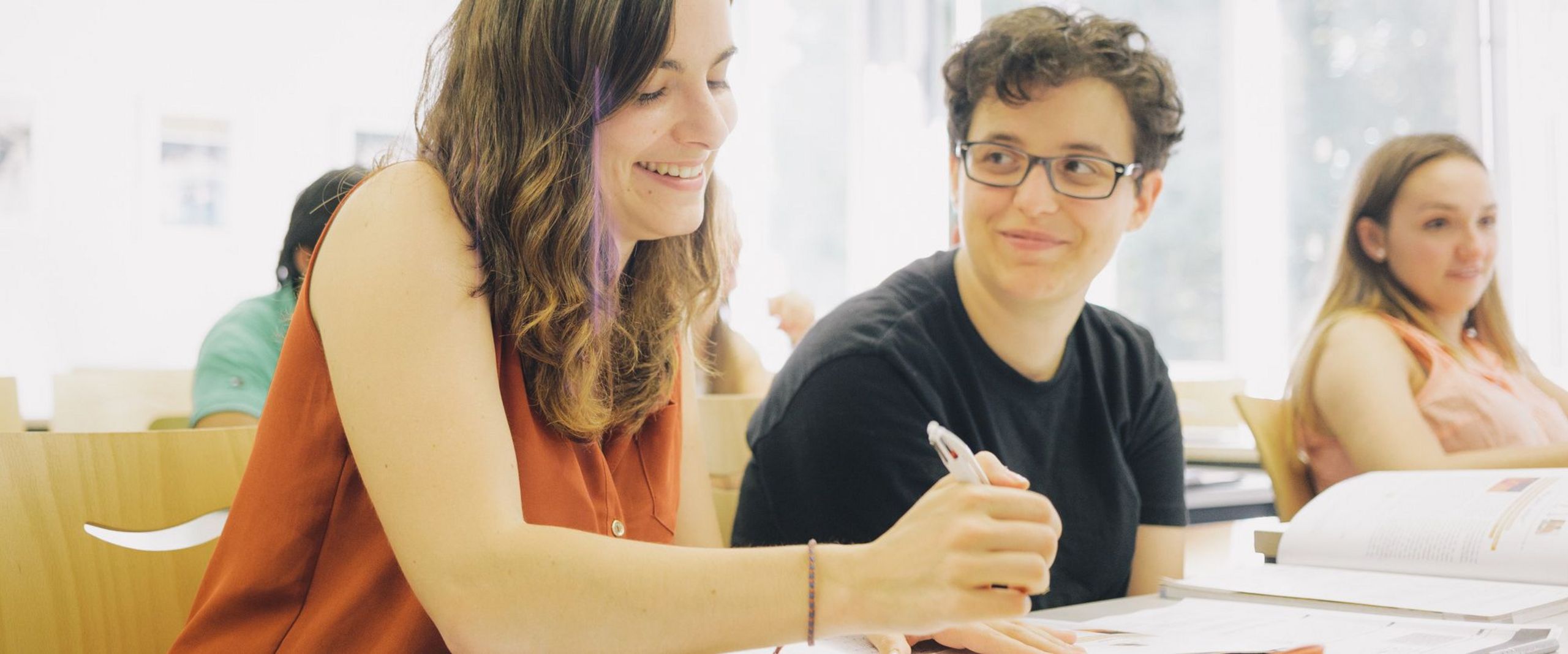 Studierende sitzen nebeneinander in einer Lehrveranstaltung und machen sich Notizen.