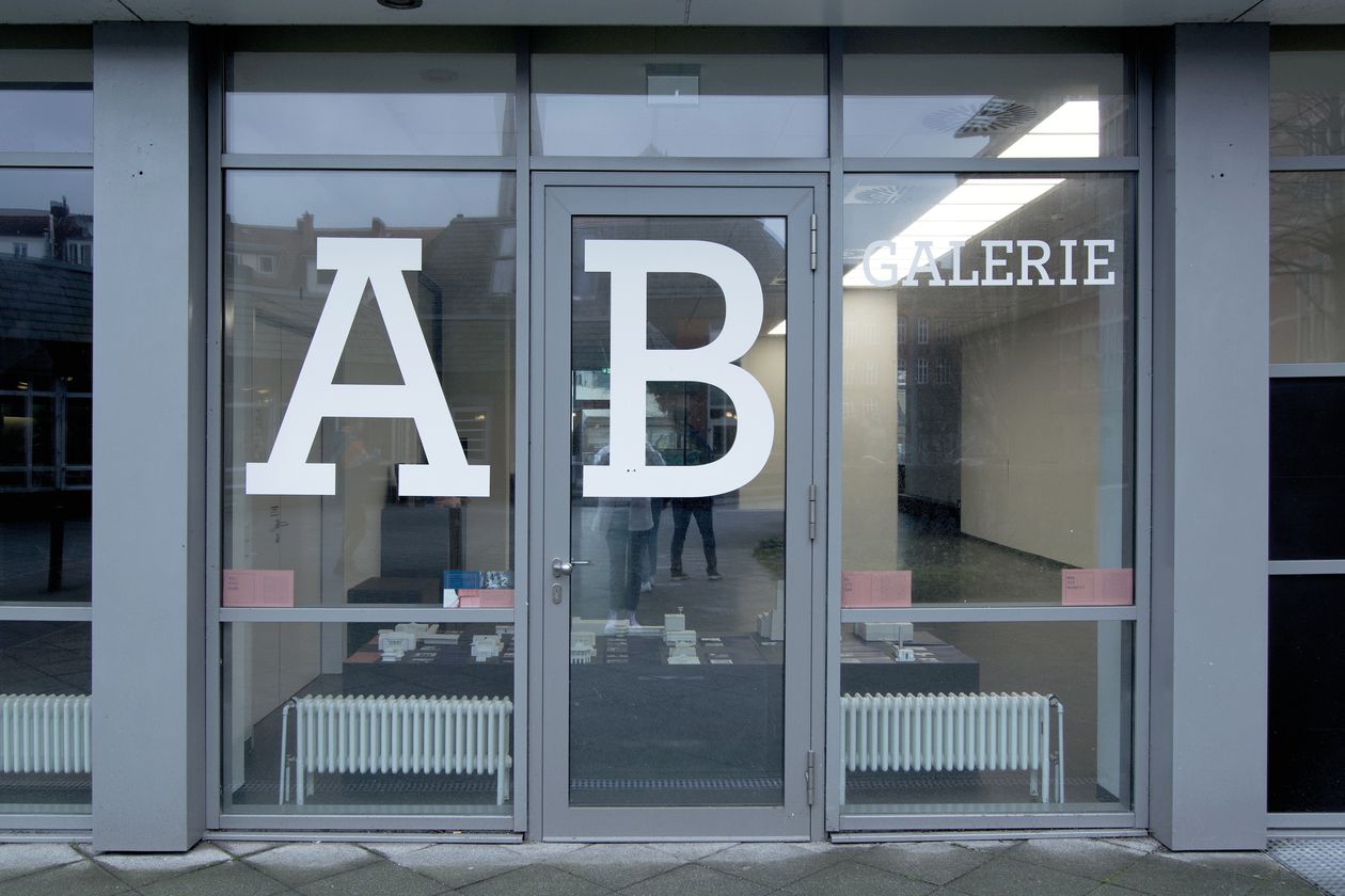 Es ist die Eingangsfassade der AB Galerie, aus einer Pfosten-Riegel-Fassade, zu sehen, wo die Ausstellung "Architektur im internationalen Kontext" stattfindet.