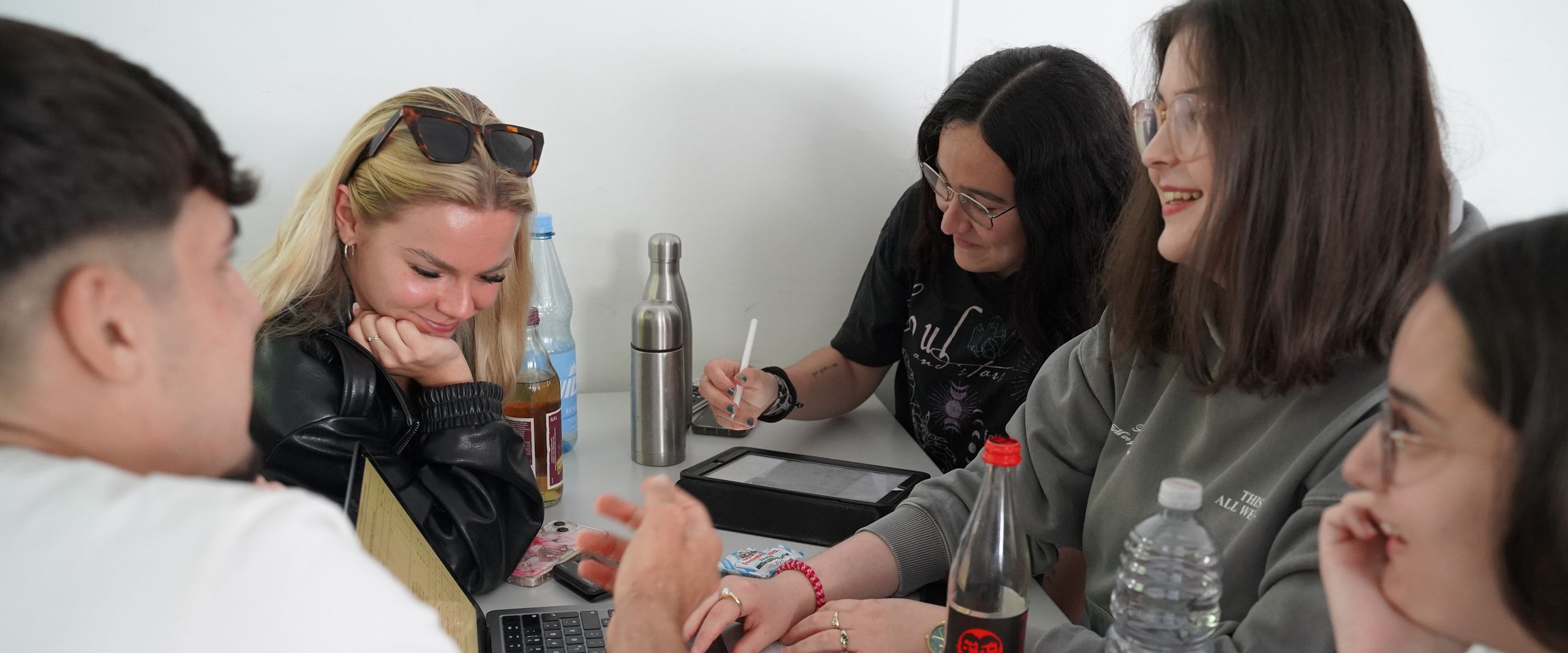 Studiernede sitzen mit Laptop am Tisch in der Runde und arbeiten zusammen.