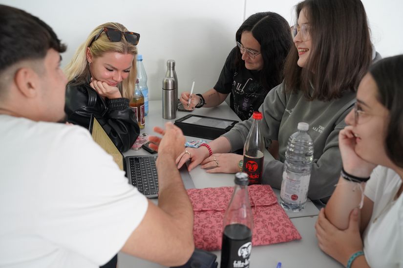 Studiernede sitzen mit Laptop am Tisch in der Runde und arbeiten zusammen.