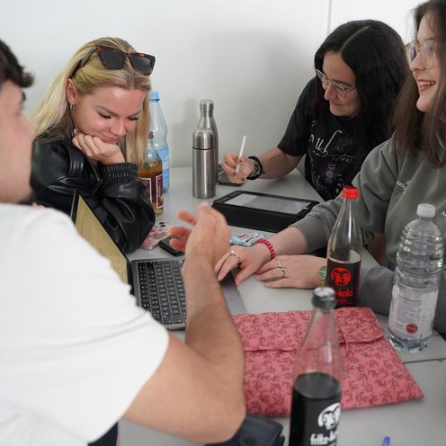 Studiernede sitzen mit Laptop am Tisch in der Runde und arbeiten zusammen.
