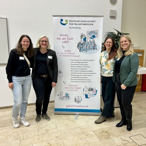 Gruppenbild mit vier Frauen. In der Mitte ein Roll-up