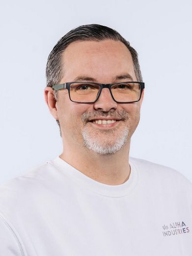 Auf dem Foto ist Martin Sebastian Barth zusehen. Er hat sein dunkles Haar zurückgelegt und trägt eine Brille und einen weißen Pullover. 