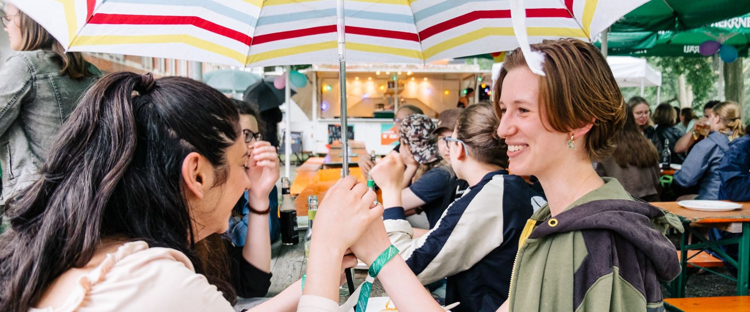 Drei Studentinnen unterhalten sich unter einem gestreiften Regenschirm. 