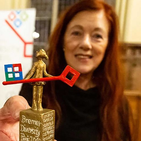 Frau h&auml;lt Skulptur in die Kamera. Im Hintergrund sieht man ein Roll-up