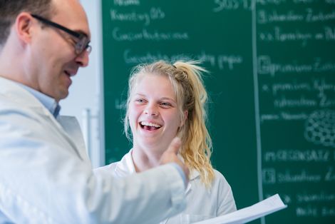 Studentin und Professor im Kittel. Sie lacht.