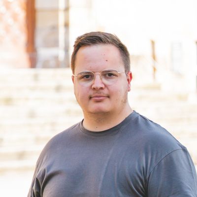 Student vor M-Gebäude und grünen Bäumen