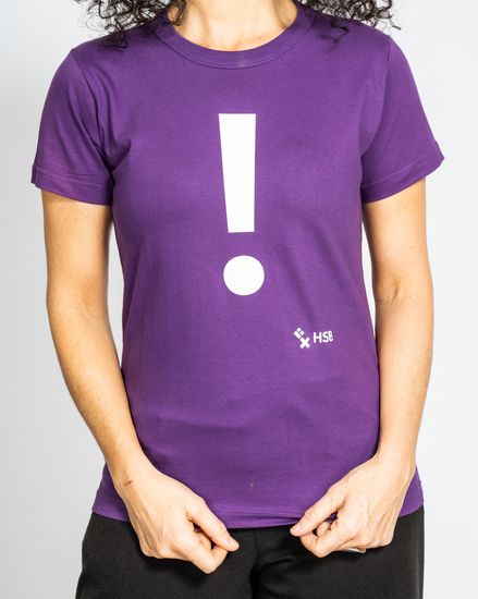 Das Model trägt ein violettes Damen-T-Shirt mit der Aufschrift “!“ und zieht es mit den Händen lang.