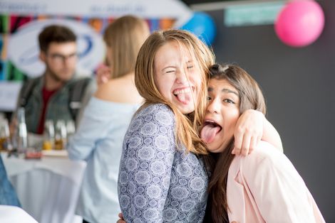 Zwei Studentinnen umarmen sich eng und schneiden Grimassen.