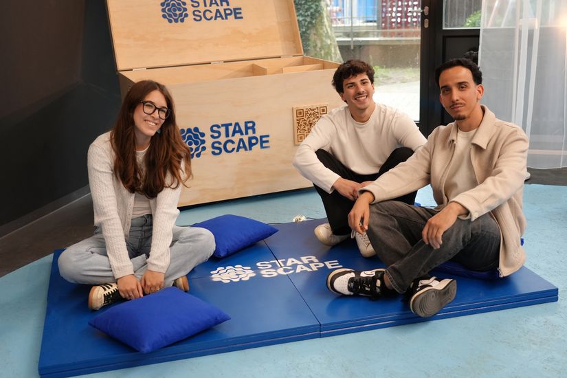 Three young people are sitting on a blue mat. Behind them is a wooden box.