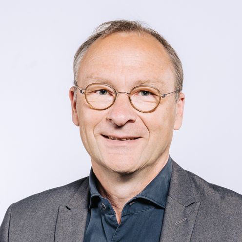 Auf dem Bild ist Rainer Hartmann zu sehen. Er hat kurzes graues Haar und eine braune runde Brille. Er tr&auml;gt ein dunkel blaues Hemd unter einem grauen Jackett. 