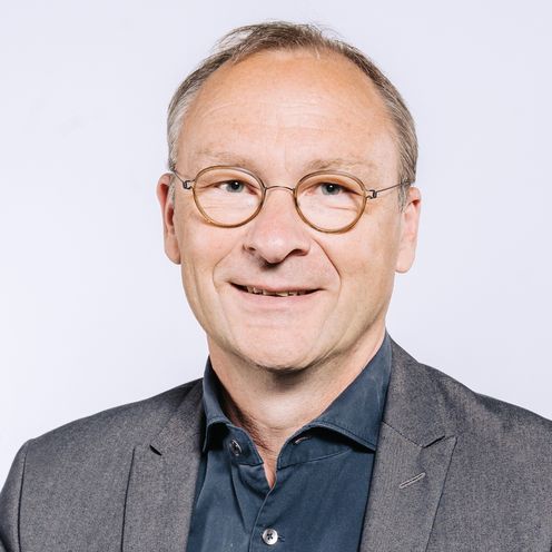 Auf dem Bild ist Rainer Hartmann zu sehen. Er hat kurzes graues Haar und eine braune runde Brille. Er tr&auml;gt ein dunkel blaues Hemd unter einem grauen Jackett. 