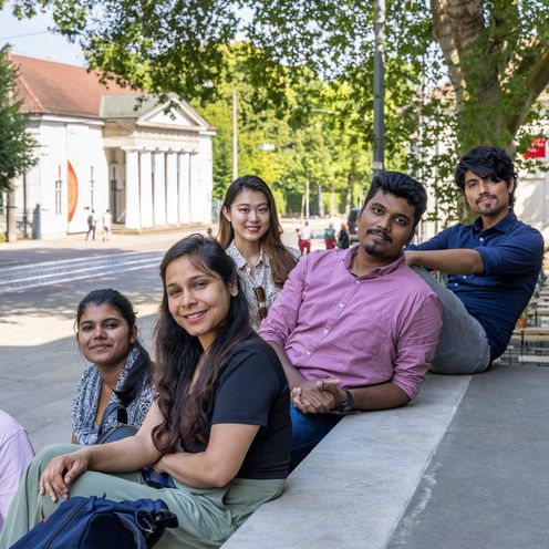 Sechs junge Menschen sitzen und stehen zusammen an einer Treppe. Im Hintergrund sieht man eine Stra&szlig;e und H&auml;user in Bremen.ch