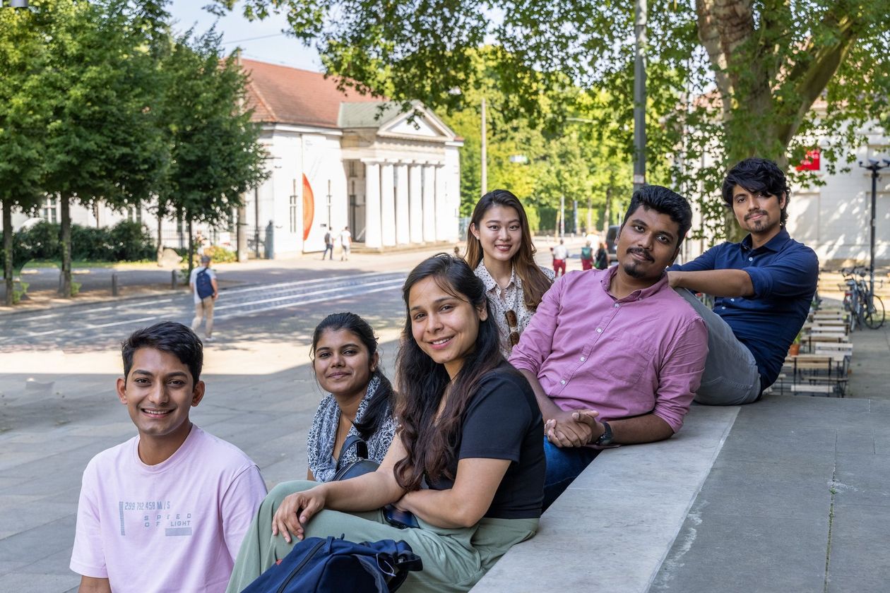 Studierende International Graduate Center  Sechs junge Menschen sitzen und stehen zusammen an einer Treppe. Im Hintergrund sieht man eine Straße und Häuser in Bremen.ch