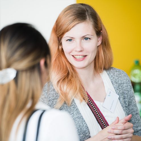 Zwei frauen unterhalten sich. Die eine schaut in die Kamera, die andere sieht man von hinten.