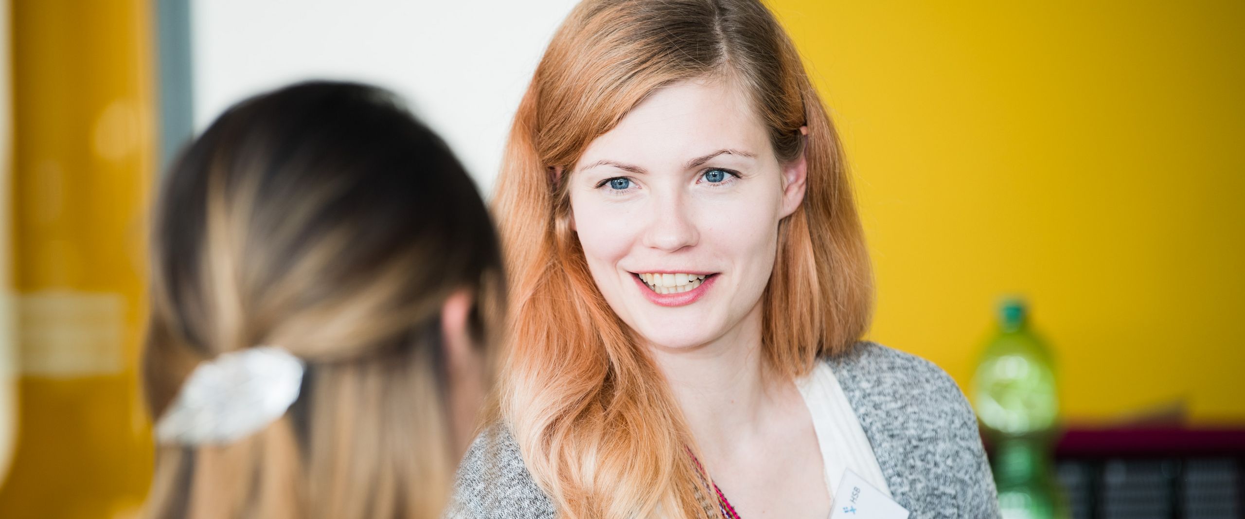 Zwei frauen unterhalten sich. Die eine schaut in die Kamera, die andere sieht man von hinten.