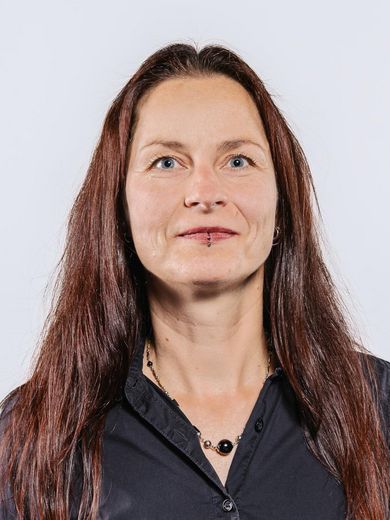 Auf dem Bild ist Juliane Wahren zusehen. Sie hat rote lange Haare und trägt eine schwarze Bluse mit einer schwarzen Kette. 