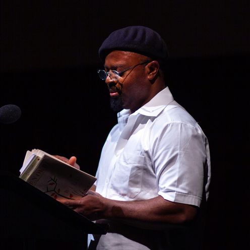 Der K&uuml;nstler Ben Okri liest auf der B&uuml;hne aus einem Buch.