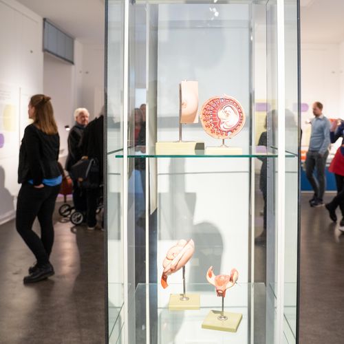 Vitrine mit Ausstellungsstücken. Im Hintergrund sieht man leute unscharf.