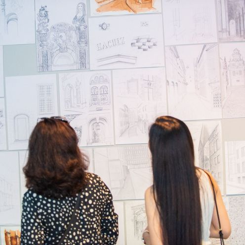 Zwei Frauen betrachten architektonische Skizzen an einer Wand. 