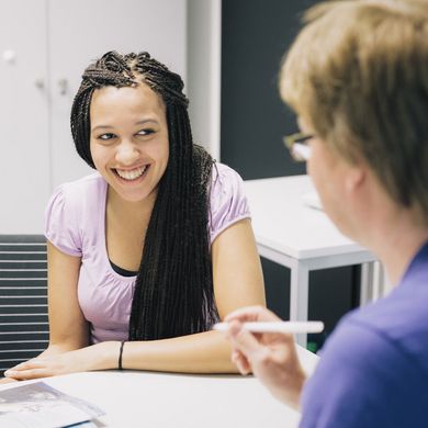 Eine Studentin und ein Studienberater sitzen sich an einem Tisch gegenüber.