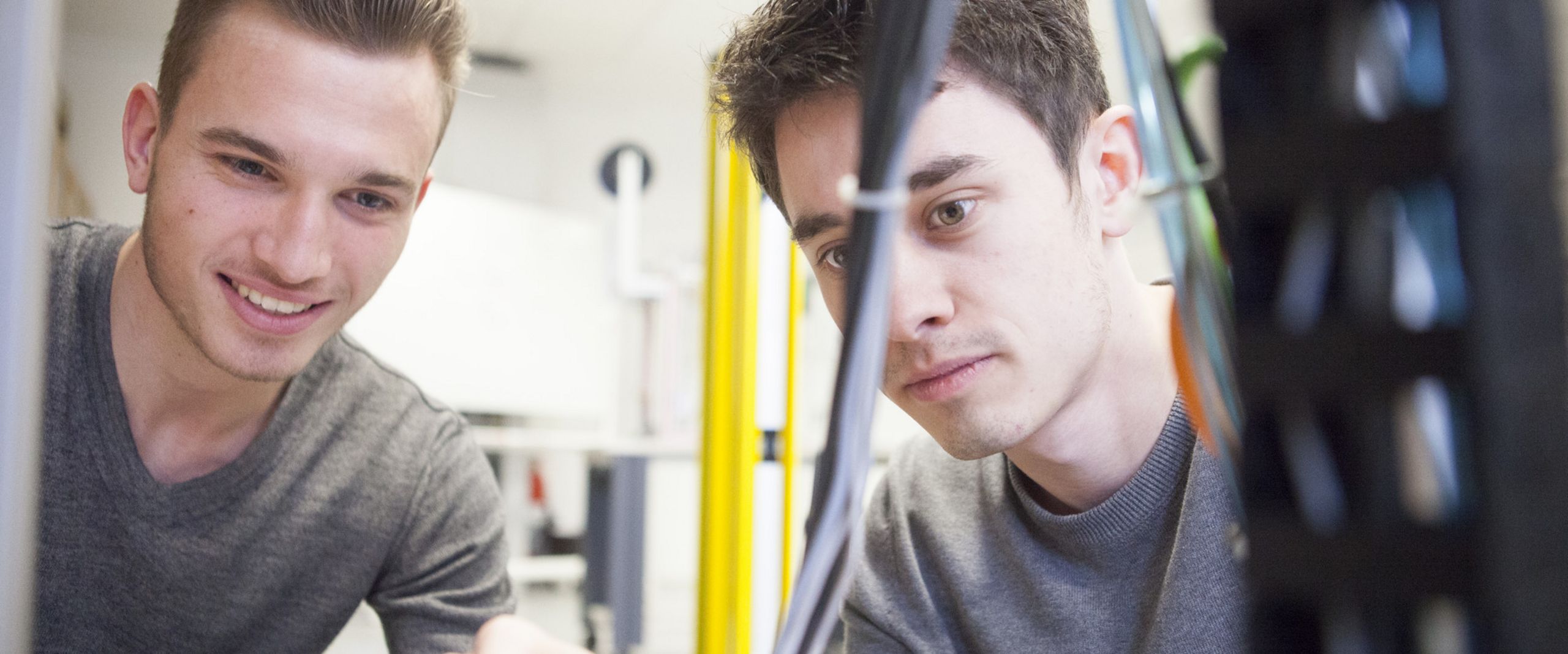 Praxis in der Vorlesung Ein Student arbeitet mit einem Schraubendreher, ein weiterer sieht ihm dabei zu.