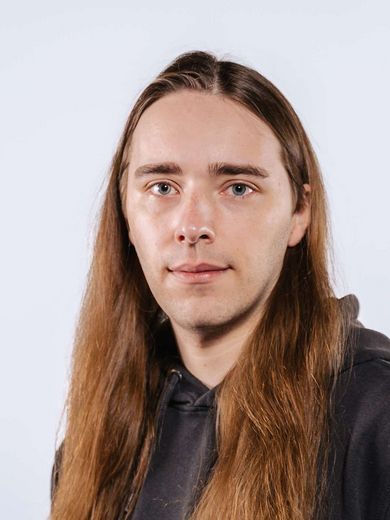 Auf dem Bild ist Nils Feske zusehen. Er hat lange braune Haare und trägt einen grauen Kaputzenpullover. 