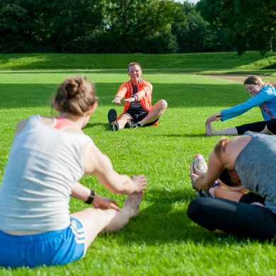 Eine Personengruppe sitzt im Kreis auf der Wiese und dehnt sich.