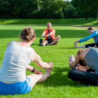 Eine Personengruppe sitzt im Kreis auf der Wiese und dehnt sich.