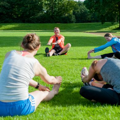 Eine Personengruppe sitzt im Kreis auf der Wiese und dehnt sich.