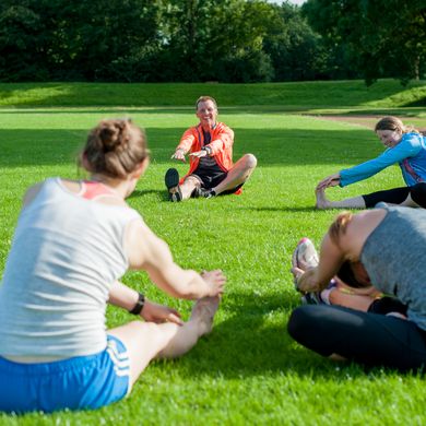Eine Personengruppe sitzt im Kreis auf der Wiese und dehnt sich.