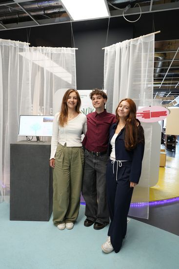  Three young people are standing in front of an exhibit and some transparent white curtains