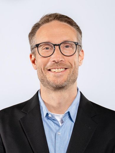 Auf dem Foto ist Peter Rickmers zusehen. Er hat kurze blonde Haare. Er tr&auml;gt eine Brille und ein blaues Hemd unter einem dunkelblauen Jackett. 