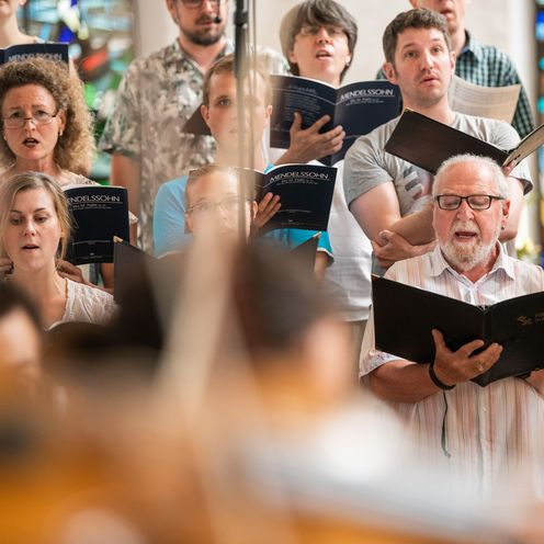 M&auml;nner und Frauen singen mit Notenb&uuml;chern in der Hand