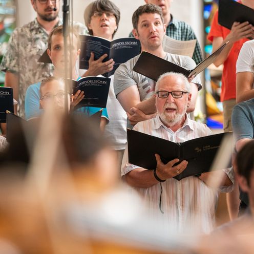 M&auml;nner und Frauen singen mit Notenb&uuml;chern in der Hand