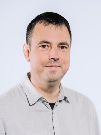 Auf dem Bild ist Daniel Matz zusehen. Er hat kurze schwarze Haare und trägt ein graues Hemd. 