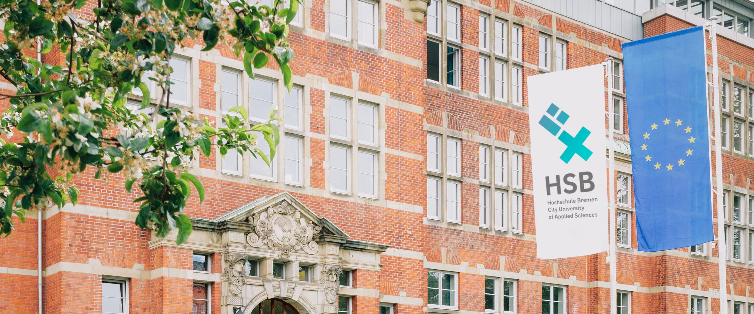 Rotes Backsteingeb&auml;ude an einer Wiese. Davor stehen Fahnen mit HSB-Logo und EU.
