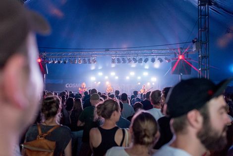 Ein großes Publikum steht vor einer Bühne in einem Zelt, auf der eine Band spielt.