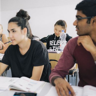 Eine Gruppe Studierender sitzt an Tischen in einem Seminarraum.