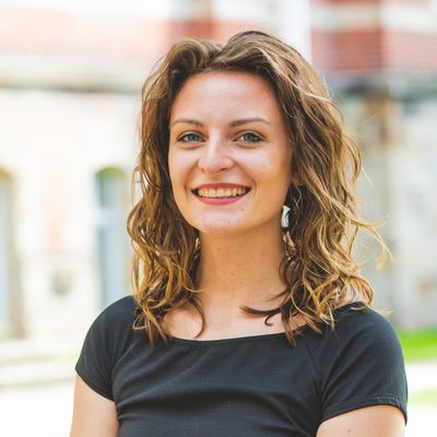 Studentin vor M-Gebäude und grünen Bäumen